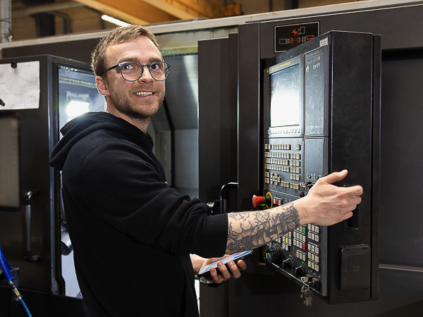 Smilende AS SCAN-medarbejder betjener en CNC-maskine