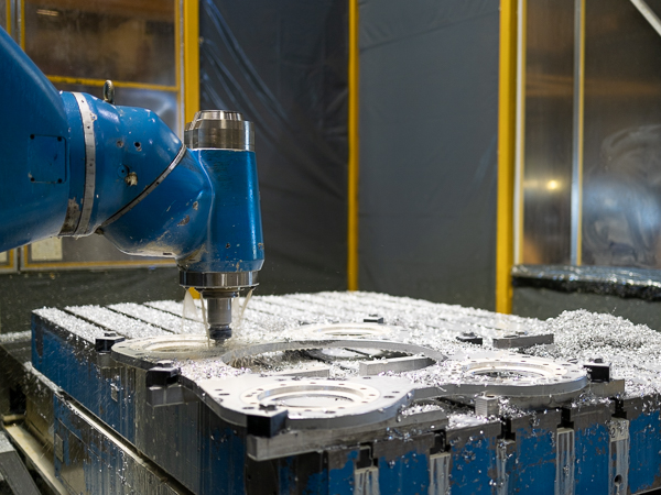 A CNC machine with a robotic arm holding a cutting tool is precisely cutting a flat sheet of metal on a worktable in a brightly lit factory