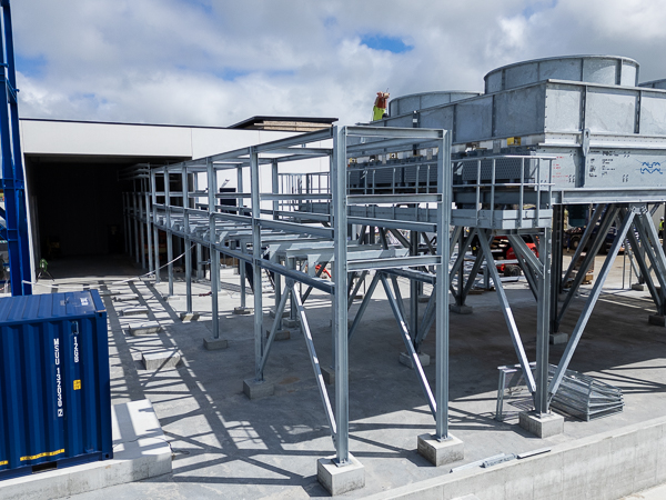 Galvanized steel structure for piping viewed from above with a cooling system and clouds in the background.