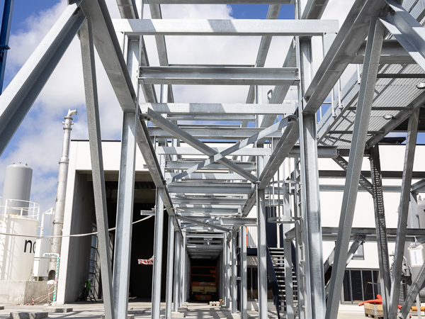 Galvanized steel structure viewed from below with blue skies and a building in the background