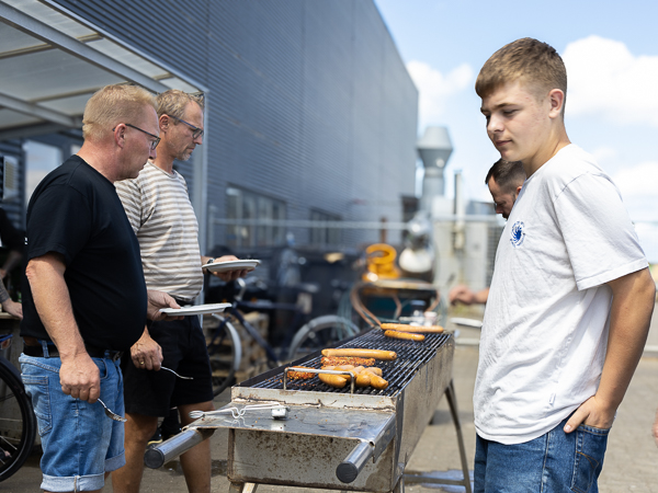 AS SCAN-medarbejdere samlet omkring en grill, der tilbereder pølser udenfor på en solrig dag.