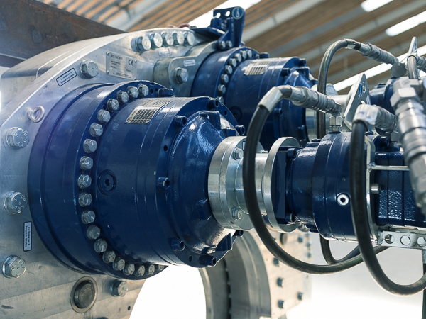 Close-up of a wind turbine gearbox assembly showing intricate mechanical details, including hydraulic connections and fast-speed turner gear components in a workshop environment.