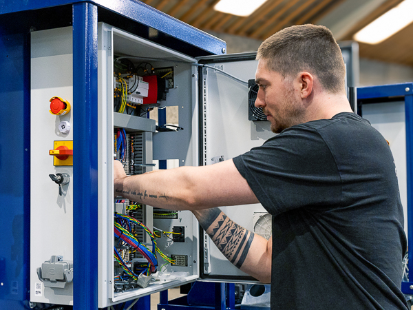 A technician working on an open electrical cabinet, inspecting and managing internal wiring and components in a workshop setting.