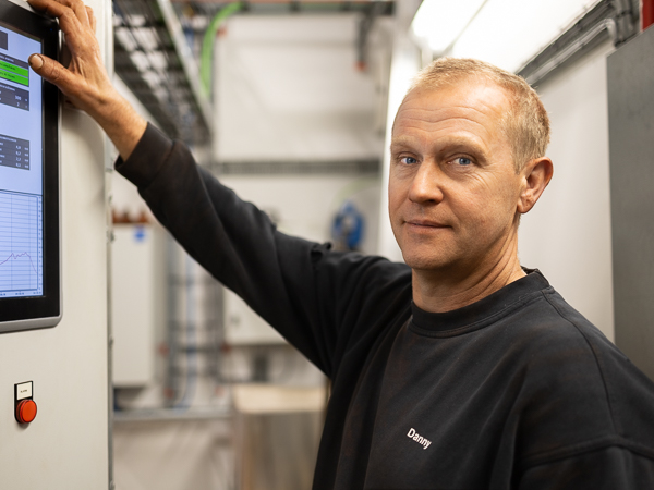 AS SCAN technician at a control panel in a technical environment, wearing a sweatshirt with the name "Danny."