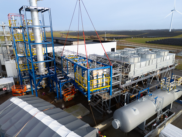 Crane lifts the process module into place at the facility, surrounded by pipes and cooling units.