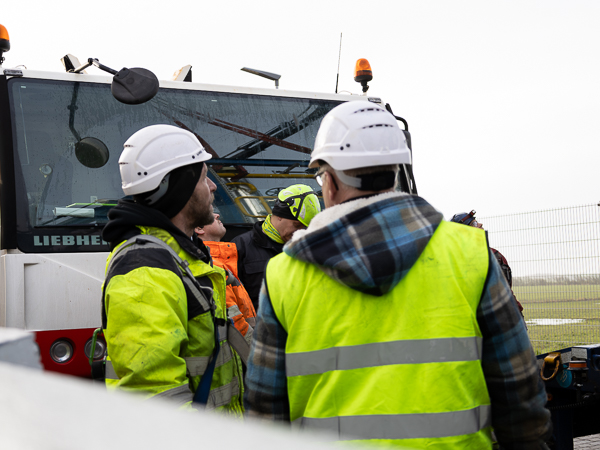 Workers in safety gear and helmets conversing in front of a Liebherr crane.