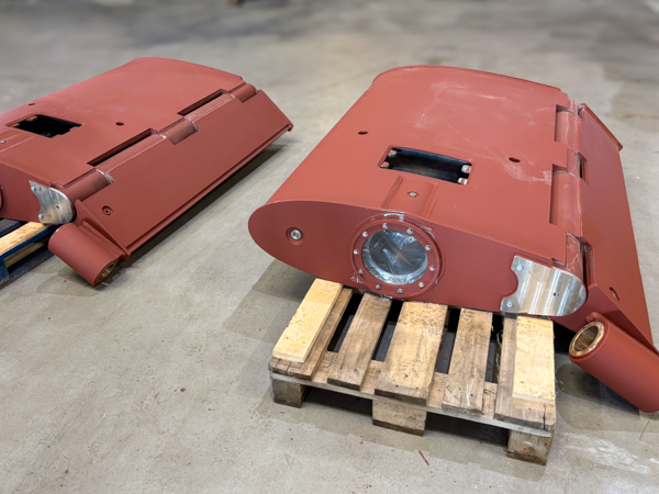 Two large, red-painted metal industrial components are resting on wooden pallets in a warehouse.