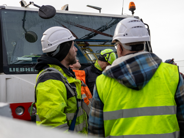 AS SCAN service technicians wearing safety gear discussing a lifting operation beside a Liebherr crane during an on-site installation.