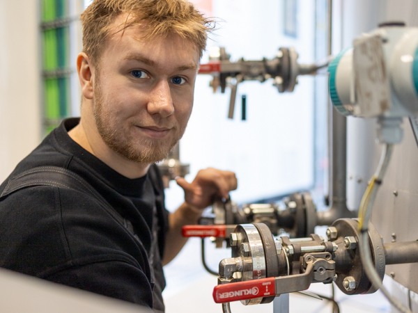 AS SCAN technician performing inspection and adjustment of industrial valves and instrumentation in a workshop setting.