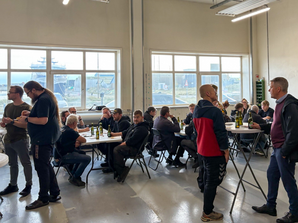 Employees talking at high tables in the workshop, with others seated at tables in the background during AS SCAN’s Friday gathering.