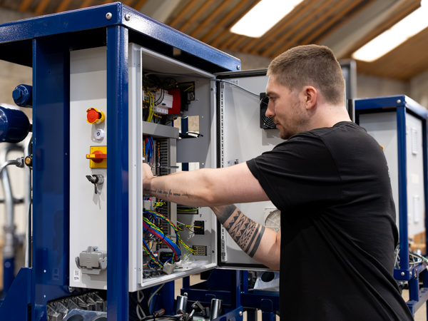 Technician working inside an open Turner Gear control cabinet, adjusting wiring and hydraulic components during Turner Gear training at the AS SCAN workshop.