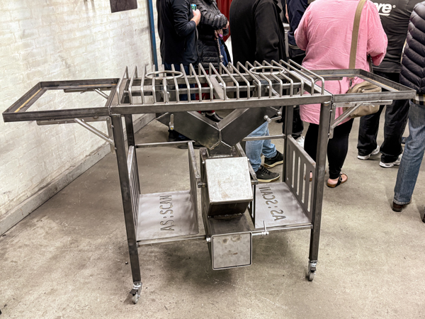 Martin’s steel barbecue trolley with a cooking grate, side tables, wheels and the AS SCAN logo cut into the lower shelves.